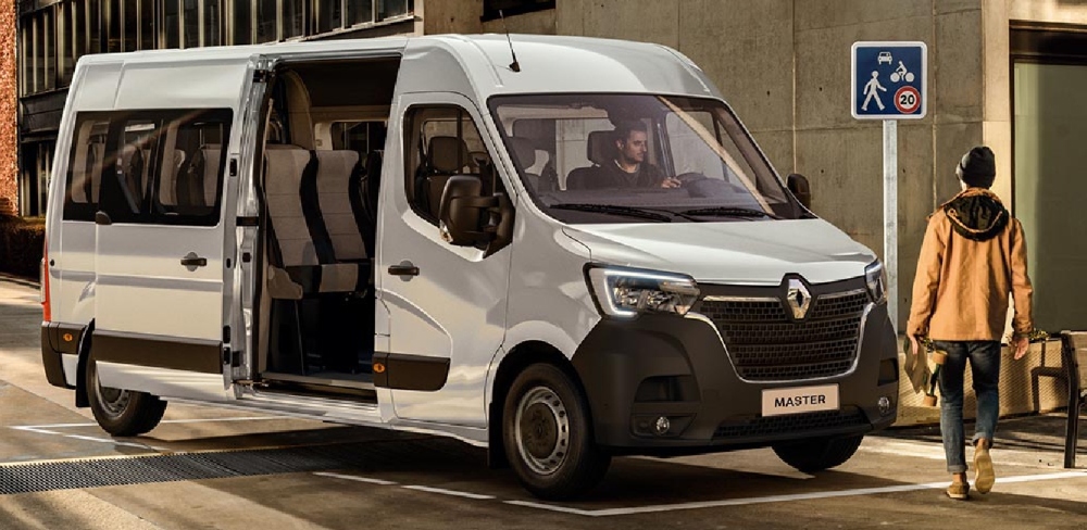 Furgón Mini bus Renault color blanco con la puerta lateral abierta y personas alrededor.